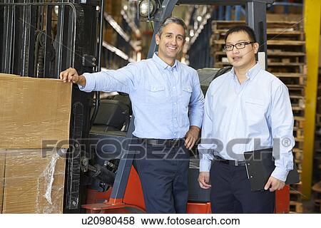 Stock Photo - Portrait Of Businessmen With Fork Lift Truck In Warehouse. Fotosearch