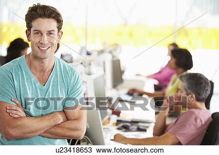 Stock Image - Portrait Of Man Standing In Busy Creative Office. Fotosearch