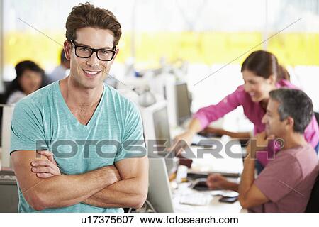Stock Photo - Portrait Of Man Standing In Busy Creative Office. Fotosearch