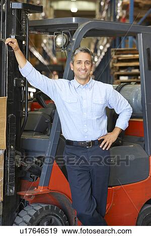 Stock Photo - Portrait Of Man With Fork Lift Truck In Warehouse. Fotosearch