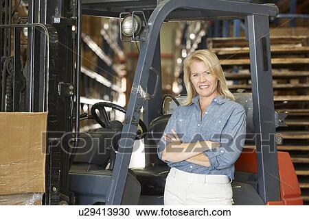 Stock Image - Portrait Of Woman With Fork Lift Truck In Warehouse. Fotosearch