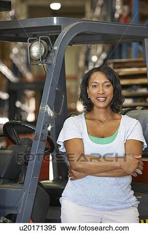 Stock Photography - Portrait Of Woman With Fork Lift Truck In Warehouse. Fotosearch