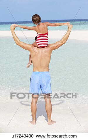 Stock Image - Rear View Of Father Carrying Daughter On Beach Holiday. Fotosearch