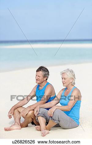 Stock Photograph - Senior Couple In Sports Clothing Relaxing On Beautiful Beach. Fotosearch