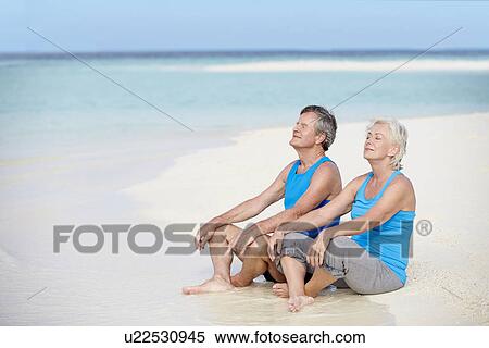 Stock Photography - Senior Couple In Sports Clothing Relaxing On Beautiful Beach. Fotosearch