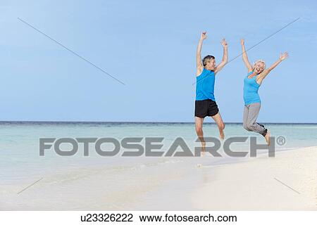 Stock Image - Senior Couple Jumping On Beautiful Beach. Fotosearch