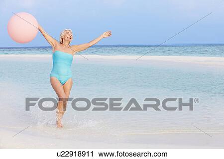 Stock Image - Senior Woman Splashing In Beautiful Sea Holding Balloon. Fotosearch