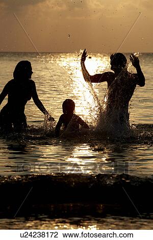 Stock Image - Silhouette Of Family Having Fun In Sea On Beach Holiday. Fotosearch
