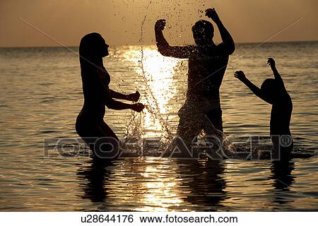 Stock Photograph - Silhouette Of Family Having Fun In Sea On Beach Holiday. Fotosearch