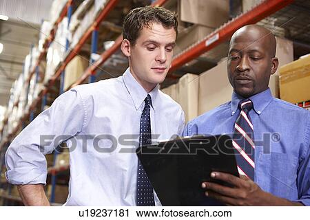 Stock Image - Two Businessmen With Clipboard In Warehouse. Fotosearch