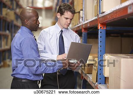 Stock Image - Two Businessmen With Laptop In Warehouse. Fotosearch
