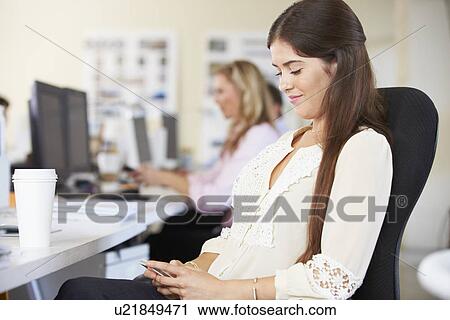 Woman Using Mobile Phone At Desk In Busy Creative Office View Large Photo Image Stock Image - Woman Using Mobile Phone At Desk In Busy Creative Office. Fotosearch