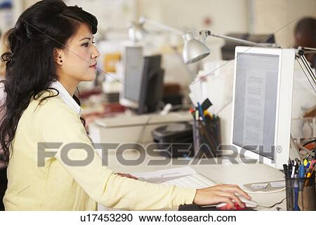 Stock Image - Woman Working At Desk In Busy Creative Office. Fotosearch