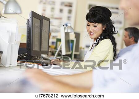 Stock Image - Woman Working At Desk In Busy Creative Office. Fotosearch