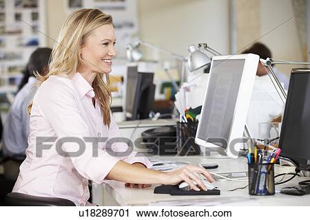 Stock Image - Woman Working At Desk In Busy Creative Office. Fotosearch