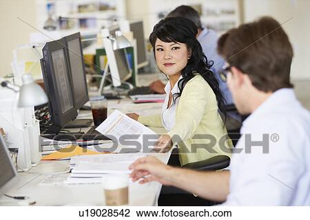 Stock Image - Woman Working At Desk In Busy Creative Office. Fotosearch