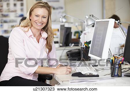 Stock Image - Woman Working At Desk In Busy Creative Office. Fotosearch