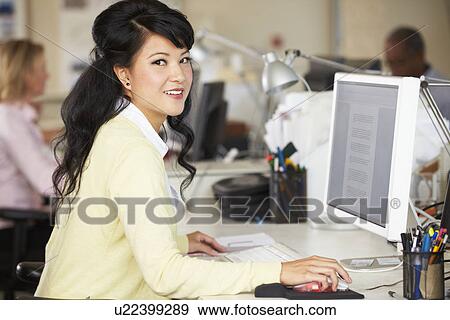 Stock Photo - Woman Working At Desk In Busy Creative Office. Fotosearch