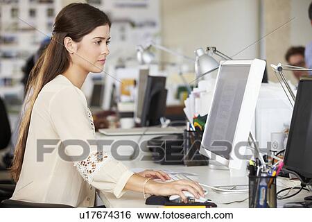 Stock Photograph - Woman Working At Desk In Busy Creative Office. Fotosearch
