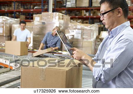 Stock Photograph - Worker Using Tablet Computer In Distribution Warehouse. Fotosearch