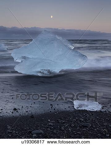 Stock Photo - Icebergs at Jokulsarlon beach, sunset with moon rising, Iceland. Fotosearch