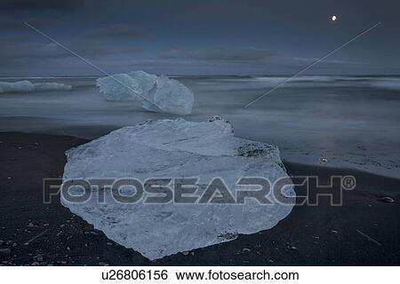 Stock Photograph - Icebergs at Jokulsarlon beach, sunset with moon rising, Iceland. Fotosearch