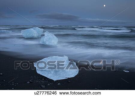 Stock Photograph - Icebergs at Jokulsarlon beach, sunset with moon rising, Iceland. Fotosearch