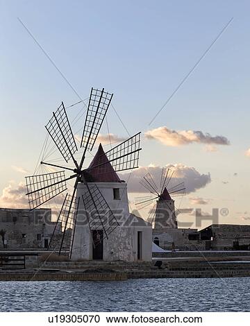 Stock Image - Windmills at Trapani saline pans, sunset, Sicily, Italy. Fotosearch