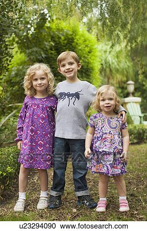 Stock Image - Brother (6-7) and sisters (2-3, 4-5) posing together in garden . Fotosearch