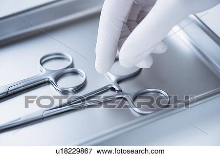 Stock Photo - Close up of hand in surgical glove choosing dental forceps, studio shot. Fotosearch