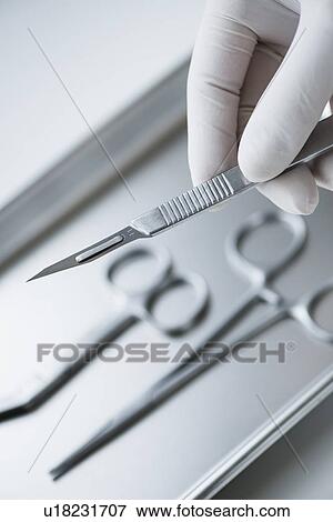 Stock Photo - Close up of hand in surgical glove holding dental scalpel, studio shot. Fotosearch