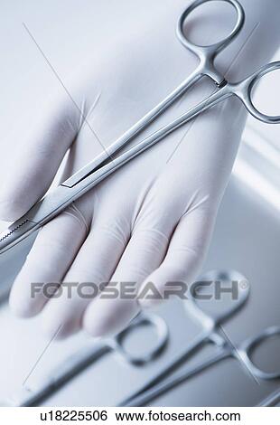 Stock Photograph - Close up of hand in surgical glove holding dental forceps, studio shot. Fotosearch