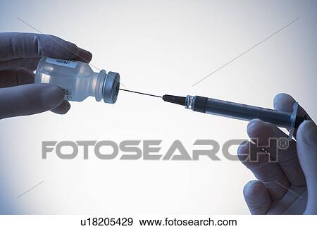 Stock Photo - Close up of hands in surgical gloves preparing syringe for injection, studio shot. Fotosearch