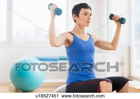 Stock Image - Mature woman exercising in gym. Fotosearch