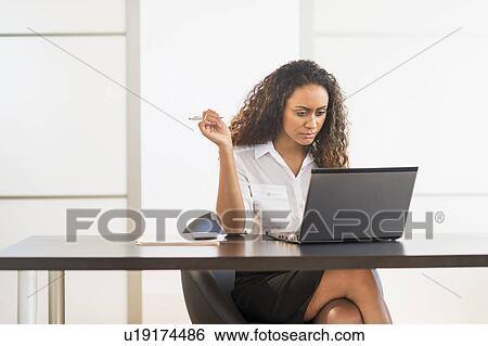 Office worker sitting by desk with laptop View Large Photo Image Stock Photograph - Office worker sitting by desk with laptop. Fotosearch