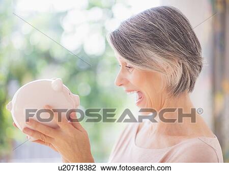 Stock Image - Portrait of excited woman holding piggy bank. Fotosearch