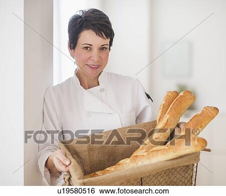 Stock Photograph - Portrait of mature woman holding basket with baguettes. Fotosearch