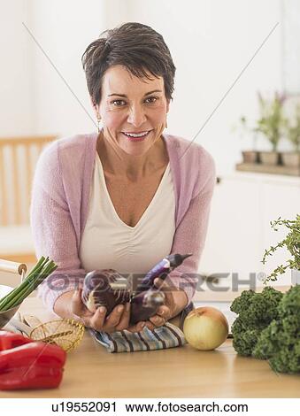 Stock Image - Portrait of mature woman in kitchen. Fotosearch