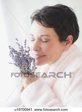 Stock Image - Portrait of mature woman smelling flowers. Fotosearch