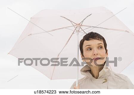 Portrait of smiling woman wearing raincoat and holding umbrella View Large Photo Image Stock Image - Portrait of smiling woman wearing raincoat and holding umbrella. Fotosearch