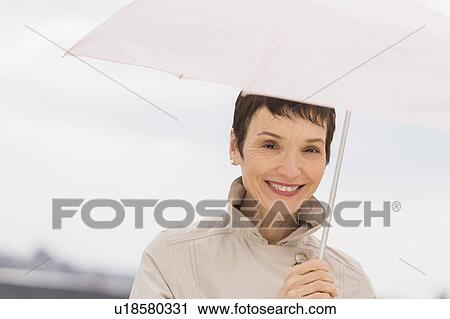Portrait of smiling woman wearing raincoat and holding umbrella View Large Photo Image Stock Image - Portrait of smiling woman wearing raincoat and holding umbrella. Fotosearch