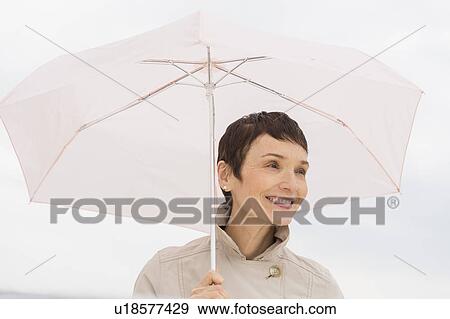 Portrait of smiling woman wearing raincoat and holding umbrella View Large Photo Image Stock Photo - Portrait of smiling woman wearing raincoat and holding umbrella. Fotosearch