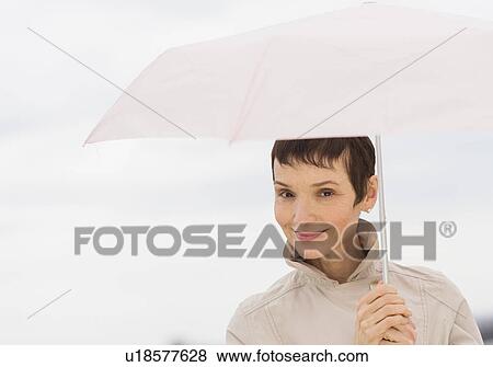 Stock Photo - Portrait of smiling woman wearing raincoat and holding umbrella. Fotosearch