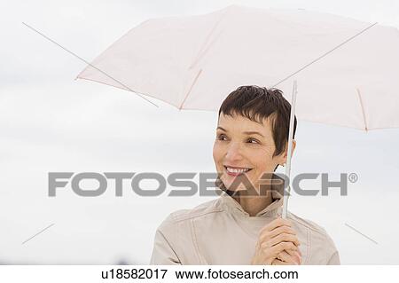 Stock Photo - Portrait of smiling woman wearing raincoat and holding umbrella. Fotosearch