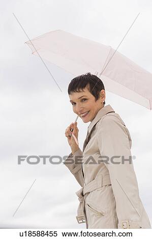 Portrait of smiling woman wearing raincoat and holding umbrella View Large Photo Image Stock Photography - Portrait of smiling woman wearing raincoat and holding umbrella. Fotosearch