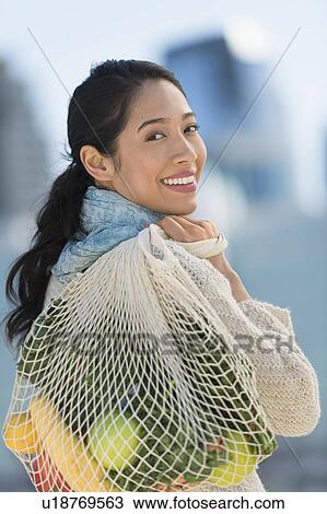 Stock Image - Portrait of smiling young woman with grocery shopping bag. Fotosearch