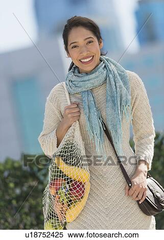Stock Photography - Portrait of smiling young woman with grocery shopping bag. Fotosearch