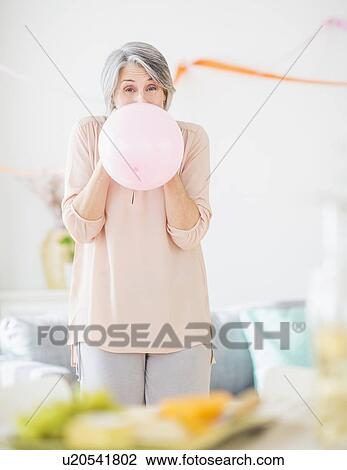 Stock Image - Portrait of woman blowing balloon. Fotosearch