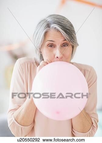 Stock Image - Portrait of woman blowing balloon. Fotosearch