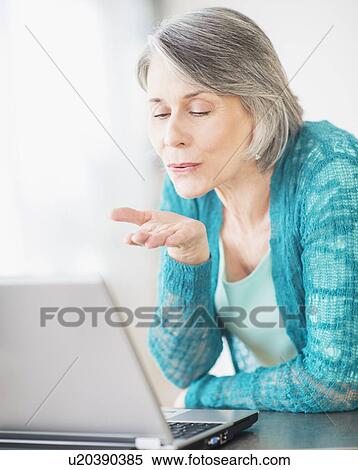 Stock Photography - Portrait of woman blowing kiss to computer camera. Fotosearch